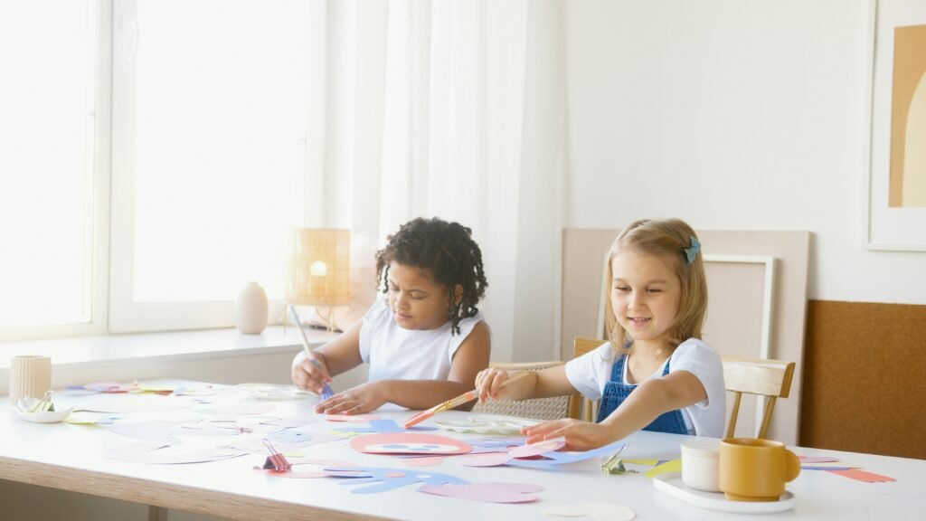 Two children engaged in creative art activities at a table indoors, expressing imagination and fun.
