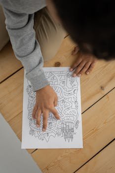 pexels-photo-7352804-7352804-1 From above of crop anonymous child sitting on floor and solving maze during weekend at home